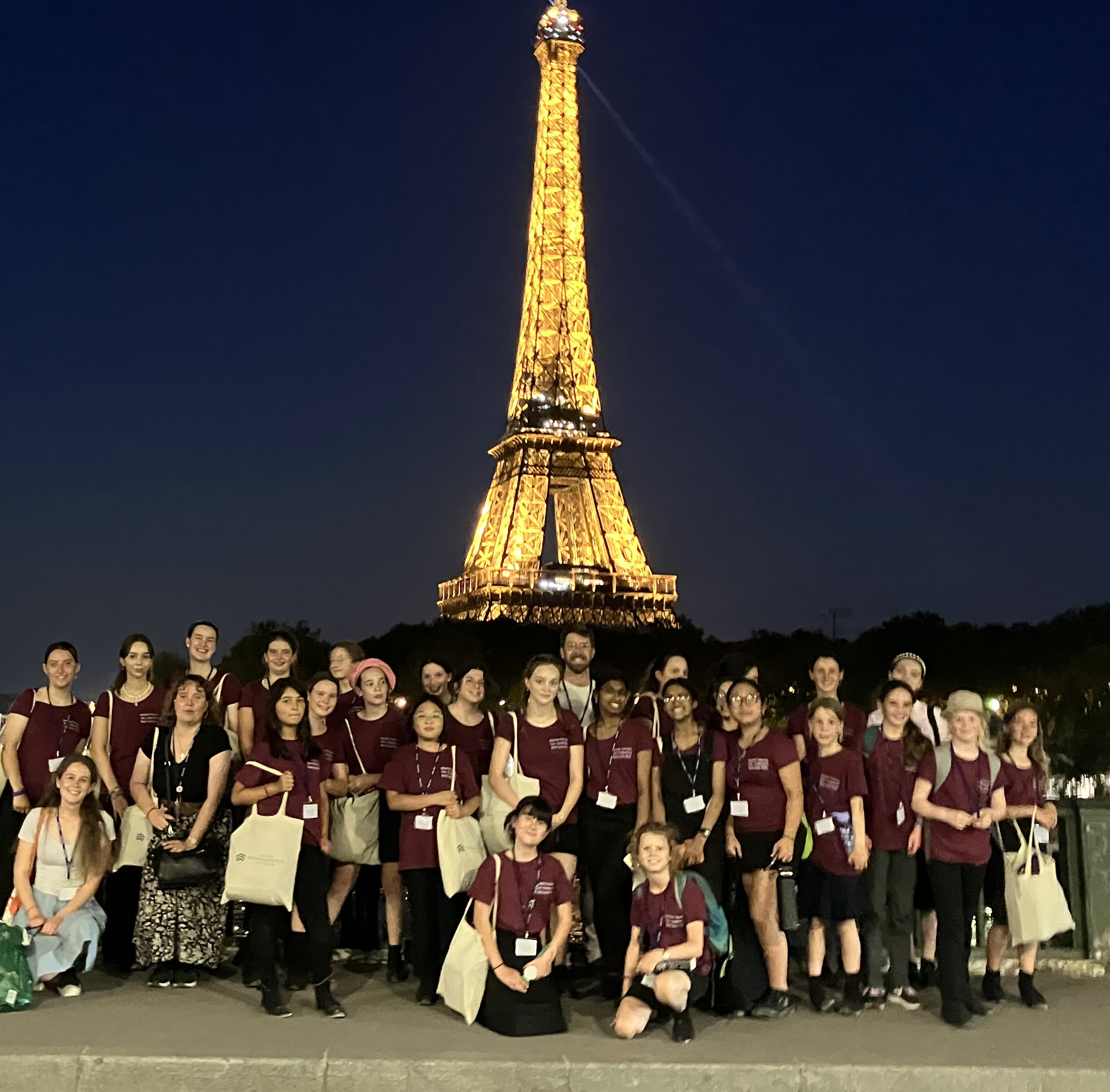 Girl Choristers stood in front of the illuminated Eiffel Tower