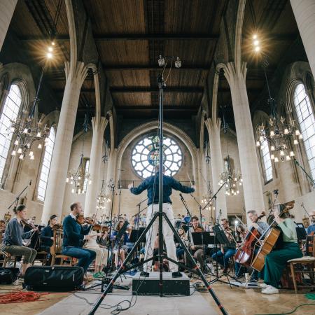Benjamin Nicholas conducts the choir and orchestra in a wooden roofed church with white columns