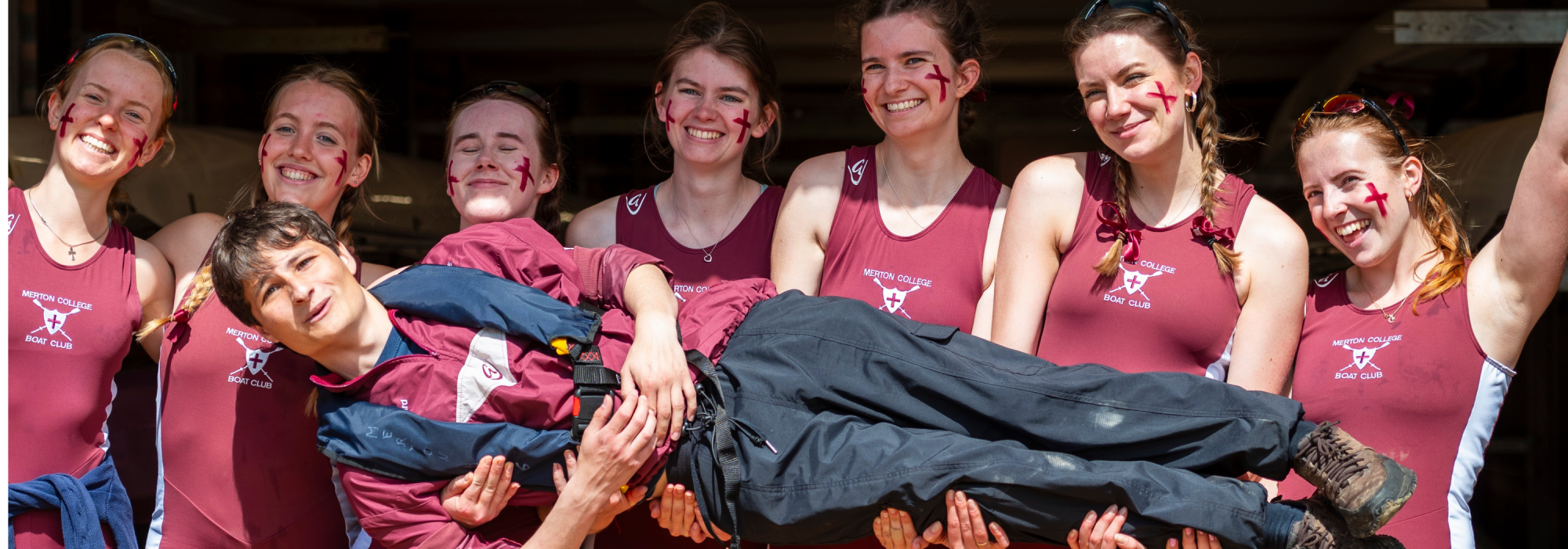 W2 celebrate their Summer VIII day 2 bump Women rowers together holding a young man on his side