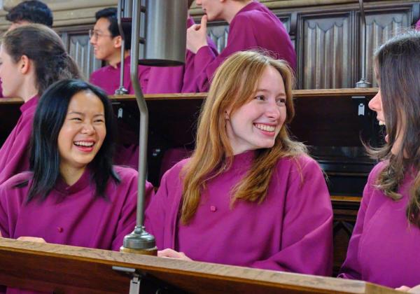 Choir members in purple robes laugh in the Choir Stalls
