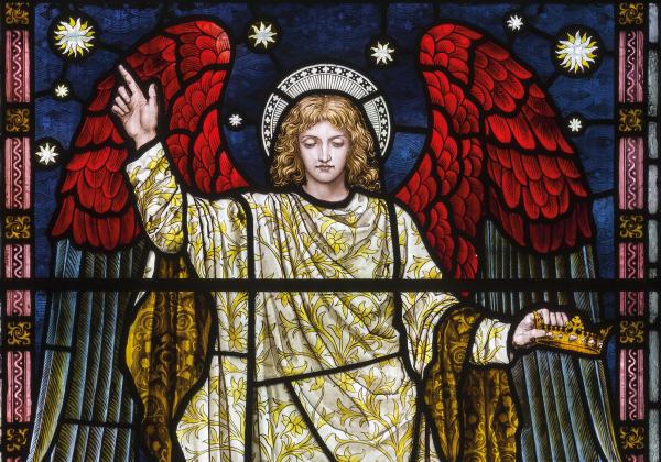 An angel with red wings and a gold robe making a symbol of peace in stained glass