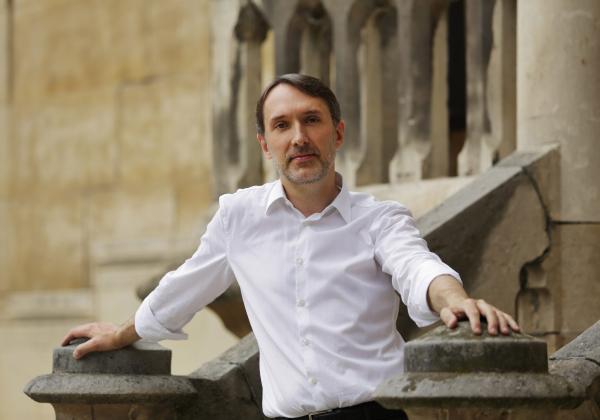 Olivier Latry Olivier Latry in a white shirt stood in front of Notre Dame in close up