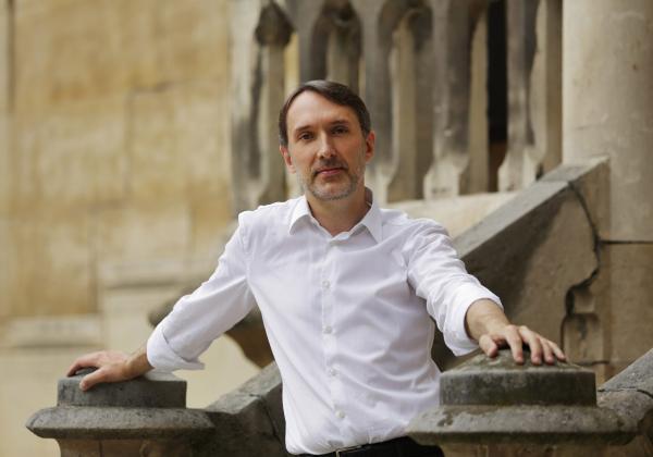 Olivier Latry in a white shirt stood in front of Notre Dame in close up