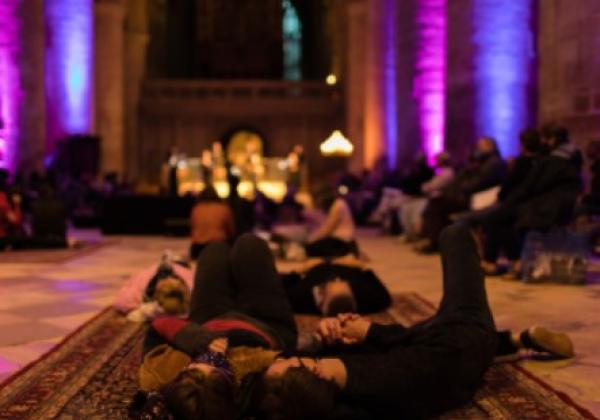 An audience in a dimly lit building lying on carpets and beanbags