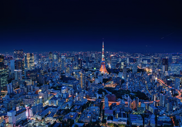 Tokyo at night: an indigo blue sky above the blue toned buildings of tokyo with orange tokyo tower glowing in the centre. A snaking path of red orange light amongst the skyscrapers shows the highway. 