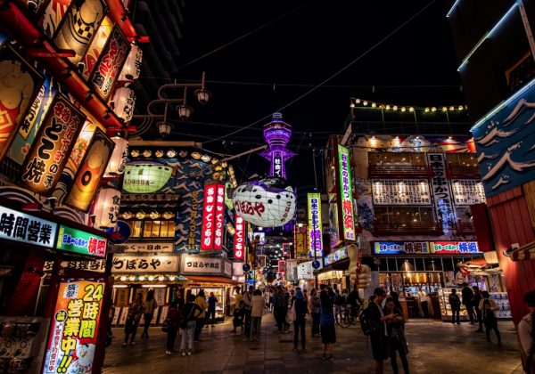 The chaotic neon lights of Osaka layered in red, green, yellow and blue in front of the purple illuminated Osaka Tower 