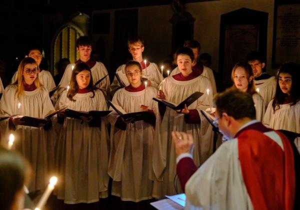 Choir lit by candles singing in white robes in the dark ante chapel