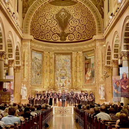 The choir in black concert dress sing a concert to a full audience in a beautiful gold mosaic church