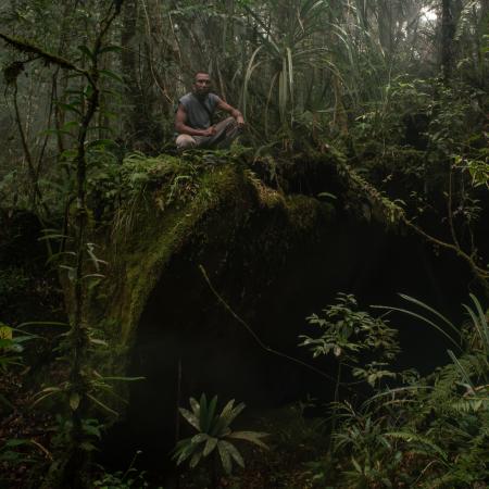 Local guide Zacharias Sorondanya sitting on top of the entrance to a cave complex in the forest